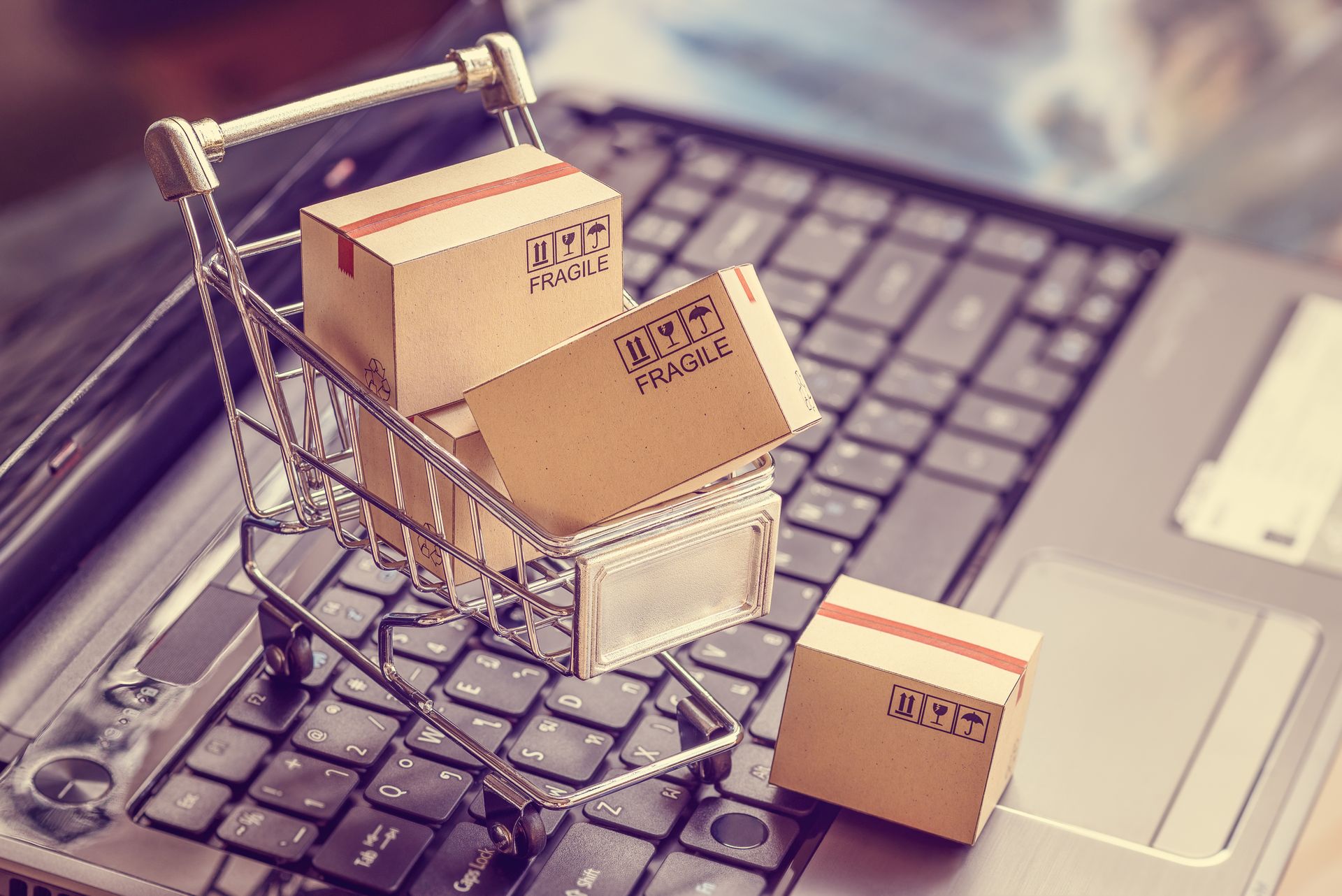 Mit Paketen gef&uuml;llter Miniatur-Einkaufswagen, der auf einer Laptop-Tastatur steht.
