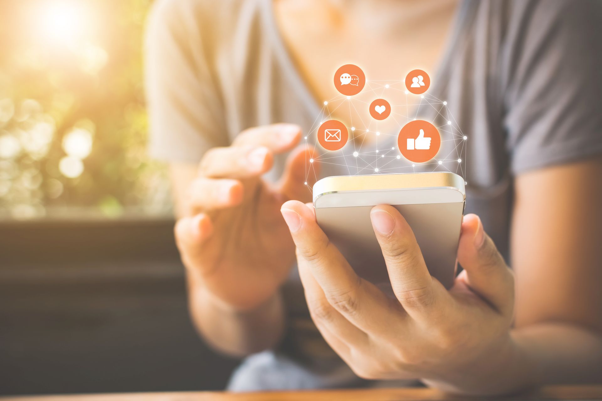 Fotoausschnitt einer Frau mit einem Smartphone in der Hand. &Uuml;ber dem Smartphone sind Icons wie Daumen-hoch, Herz und ein Brief in einem fast transparenten Netz verbunden.
