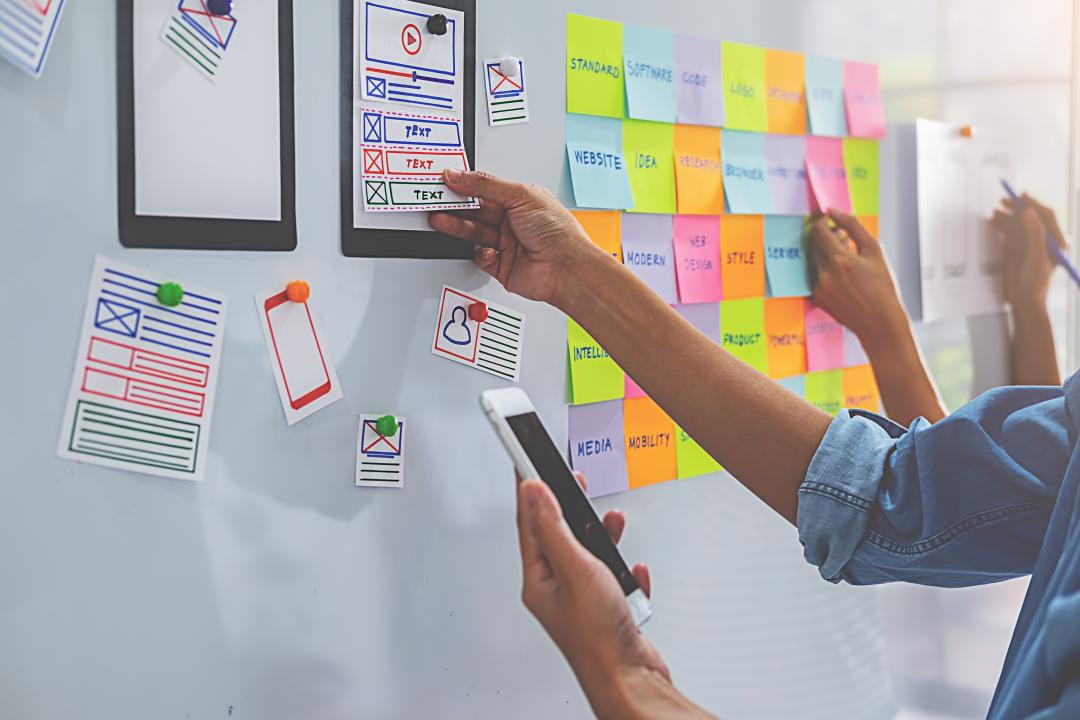 Foto eines Whiteboards, auf dem mehrere Personen gemeinsam Ideen f&uuml;r das Design einer App sammeln